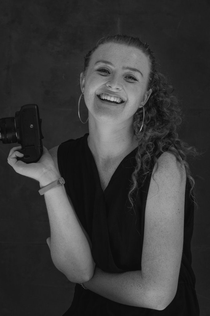 Portrait taken of photographer, S Brazier Photography. The portrait is in black and white and she is holding a camera. About S Brazier Photography