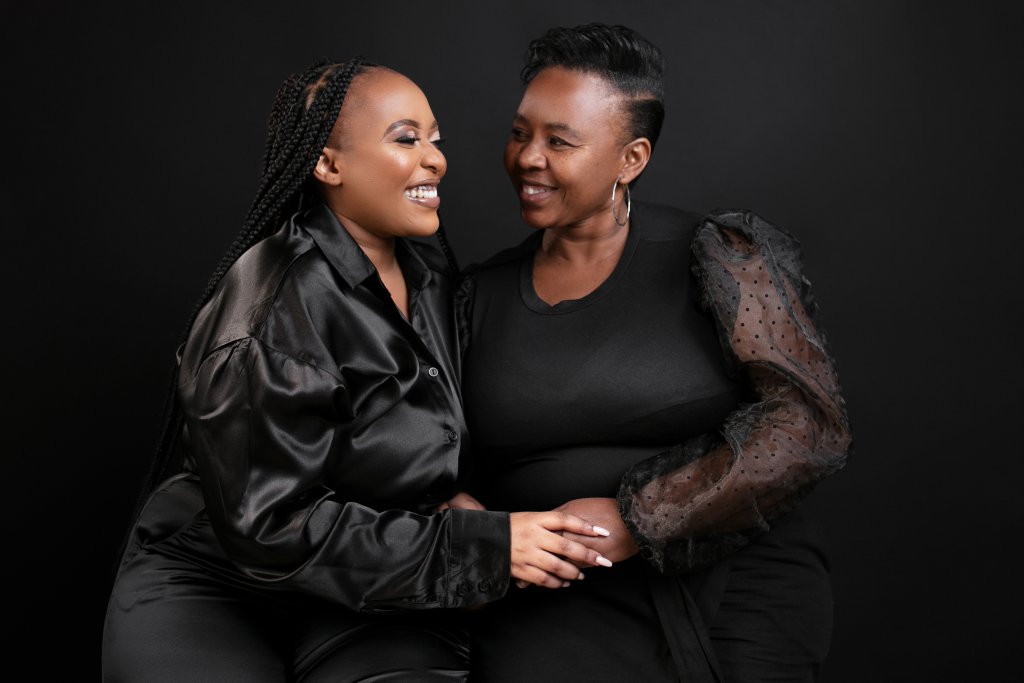 Mother and daughter sharing a moment during a photoshoot. They are both wearing black.